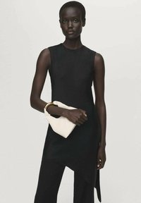 Vestido negro sin mangas con un dobladillo asimétrico, combinado con un bolso de mano blanco. La tela parece suave, creando una silueta elegante.
