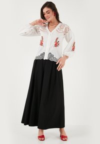 White embroidered blouse with lace details and floral patterns on sleeves, paired with a black full skirt and red sandals, showcasing contrasting colors.