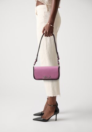 Pink leather crossbody bag with a flap closure, silver logo detail, and a detachable strap. Paired with white cropped pants and black heels.