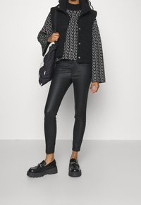 Black faux fur vest over a patterned black and white long-sleeve top, paired with black leather pants and chunky black loafers.