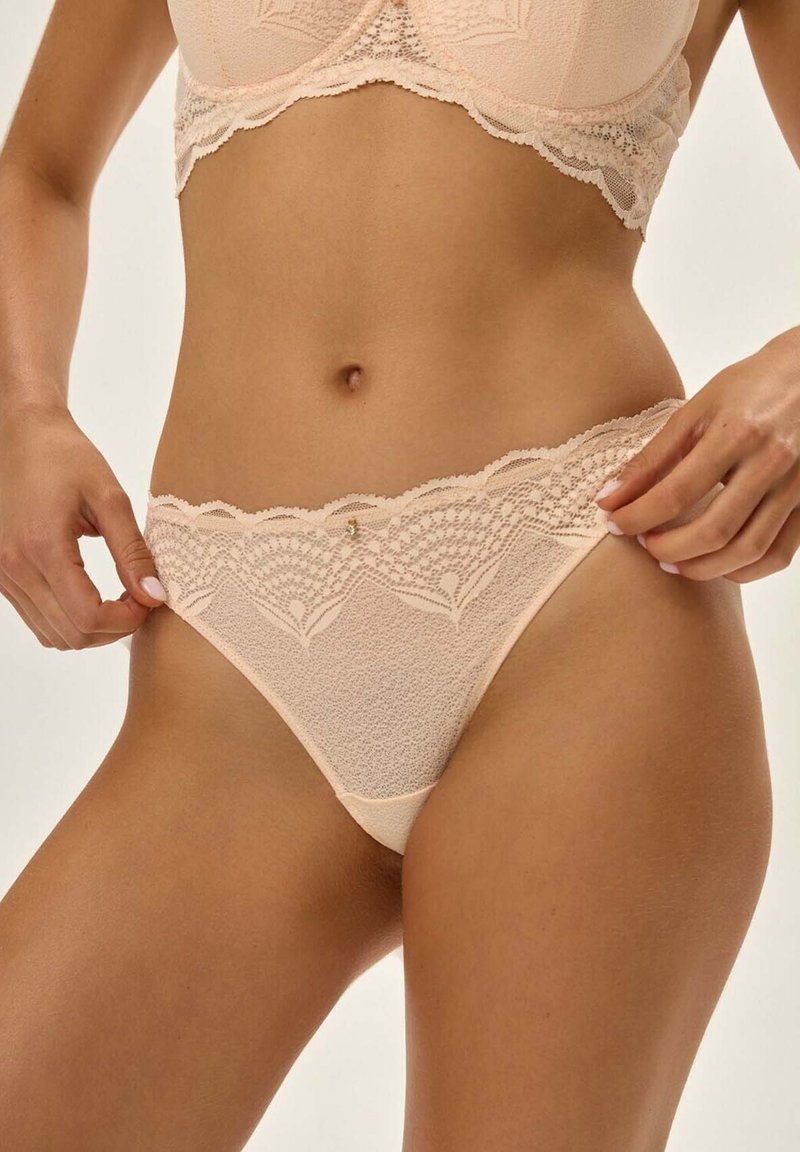 Nude-String mit Spitzenbesatz, der einen strukturierten Stoff mit floralem Muster und einem kleinen Akzentdetail am Bund aufweist.