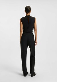 Schwarzes �ärmelloses Top mit einem Schlüssel-Ausschnitt am Rücken, kombiniert mit eng anliegenden schwarzen Hosen. Glatter Stoff mit einem eleganten, minimalistischen Design.