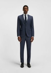 Marinblå kostym i texturerad tyg, med enbladsblazer, snedskurna ficklappar och slim-fit byxor. Svarta dress skor fulländar looken.