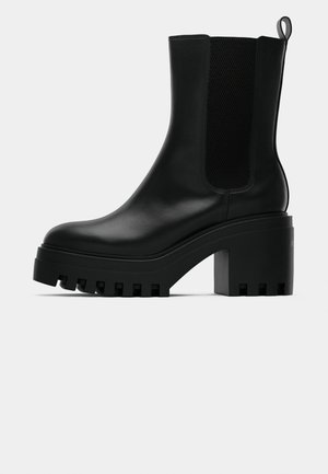 Sorte lær ankelstøvle med rund tå, chunky plattformsåle og mesh-sider. Har en pull-tab for enkel påføring.