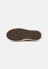 Rubber sneaker outsole in brown with textured patterns. Features include geometric designs and a contrasting cream-colored edge.