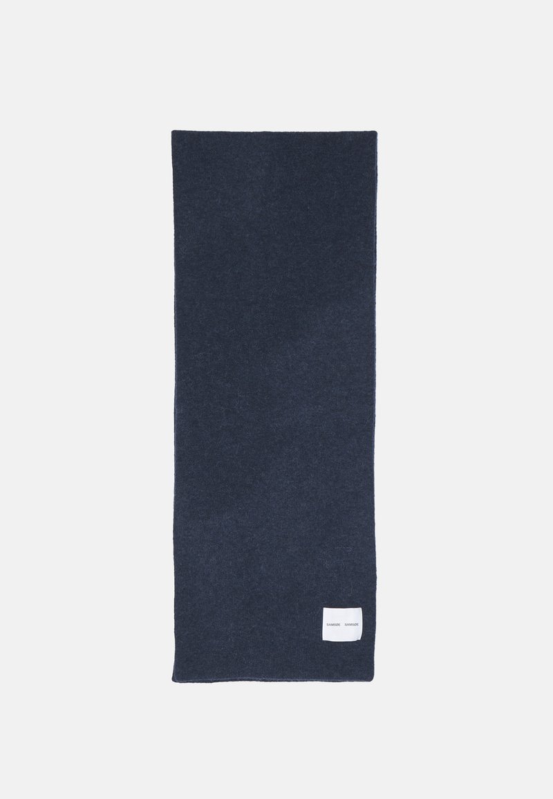 Écharpe en laine bleu marine avec une texture douce, de forme rectangulaire, et une petite étiquette blanche dans le coin inférieur droit.