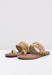 Litteet sandaalit, joissa on beige pohja, koristeltu kultaisilla ja hopeisilla nauhoilla sekä varvaslenkillä. Pehmeä, teksturoitu pohja mukavuutta varten.
