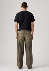 Τζιν παντελόνια με φαρδύ πόδι σε ξεθωριασμένο μπεζ χρώμα με σκούρες λεπτομέρειες, διαθέτουν κλασικό σχέδιο με πέντε τσέπες και λογότυπο πίσω. Μαύρο μπλουζάκι από πάνω.