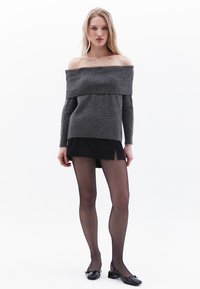Sweter w kolorze ciemnoszarym, z dekoltem off-the-shoulder, prążkowany, z długimi rękawami, zestawiony z czarną mini spódnicą oraz przezroczystymi czarnymi rajstopami, dopełniony czarnymi płaskimi butami.