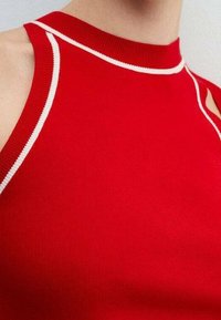 Rotes ärmelloses Oberteil mit weißer Einfassung entlang des hohen Ausschnitts und der Armlöcher, zeigt nackte Schultern und oberen Brustbereich.