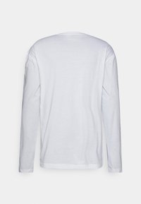 Dlouhý rukáv, tričko s kulatým výstřihem vyrobené z měkké bílé látky, s hladkým povrchem, rovným lemem a bez viditelných vzorů nebo ozdob.