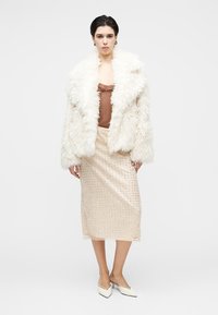 Manteau en fausse fourrure blanche, haut en satin marron, jupe crème à sequins longueur genou, et chaussures blanches à bouts pointus. Éléments de design texturés et superposés.