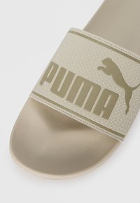 Beige rubber slide sandal with a textured strap featuring an embossed geometric pattern and a raised logo in a darker beige tone.