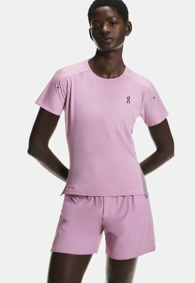 T-shirt de sport rose clair à manches courtes, logo sur la poitrine, assorti à un short. Texture lisse, tissu respirant, design fonctionnel.