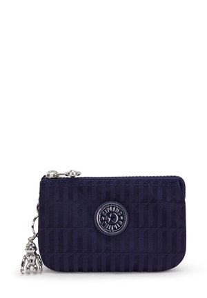 Navy zippered wallet made of textured fabric, featuring a round logo emblem and a decorative silver charm. Simple rectangular shape.
