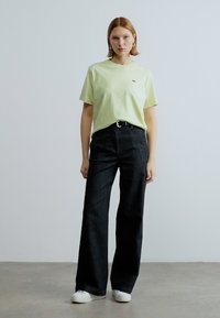 Πράσινο βαμβακερό t-shirt με μικρό λογότυπο, συνδυασμένο με μαύρο τζιν παντελόνι καμπάνα ψηλής μέσης. Άσπρα αθλητικά παπούτσια ολοκληρώνουν το ντύσιμο.