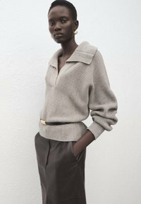 Maglione grigio chiaro lavorato a maglia con un ampio colletto, vestibilità morbida e trama a coste, abbinato a pantaloni marrone scuro a vita alta e una cintura nera.