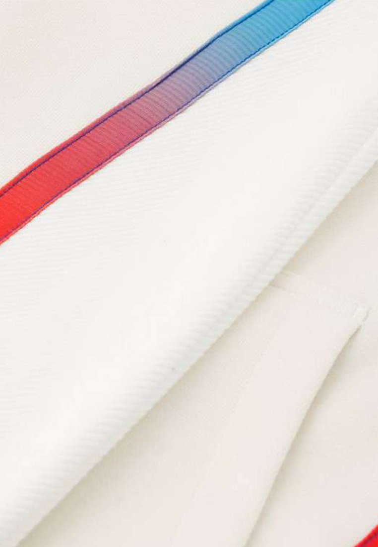 Tejido blanco con una prominente raya diagonal que transiciona de rojo a azul. La textura parece suave con un sutil canalé.