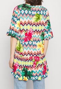 Blommig tunika med ett zickzackmönster i livfulla färger som rosa, grön och gul. Volangärmar och en kjol med volanger.