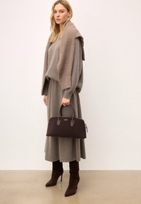 Barna bőr kézitáska dupla fogantyúkkal és arany színű kiegészítőkkel, szürke kötött pulóverrel és szoknyával párosítva, barna velúrból készült magassarkú csizmával kiegészítve.