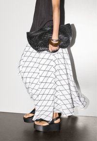 Sort vævet clutch taske, hvid nederdel med sort diamantmønster, sorte platform sandaler, lagdelte træ- og metalarmbånd.