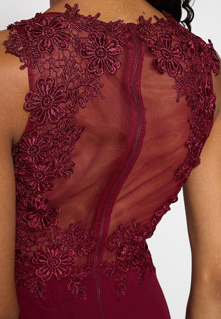 Burgundowa sukienka z bogatym haftem koronkowym w kwiatowe wzory na przezroczystych plecach. Zamek błyskawiczny w centrum biegnie pionowo wzdłuż pleców.