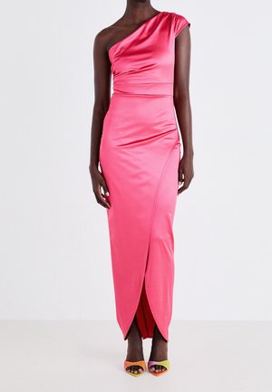 Vrouw die een roze satijnen jurk draagt met één schouder, tot op de grond reikend en een voorscheur, gecombineerd met multicolor hoge hakken sandalen.