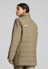 Beež puffer jakker, millel on tikandiga tekstuur ja kõrge krae. Omab külgavad ja valget Puma logo ülemisel seljal. Sile, kerge materjal.