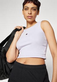 Levanduľový rebrovaný crop top s okrúhlym výstrihom a logom, kombinovaný s čiernymi teplákmi. Textúra je hladká, materiál je elastický.