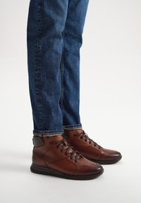 Brązowe skórzane botki za kostkę z czarnymi akcentami, okrągłymi noskami i sześcioma oczkami, połączone z niebieskimi dżinsami, lekko podwiniętymi na mankietach.