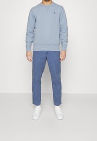 Světle modrá mikina s žebrovanými manžetami, spárovaná s tmavě modrými kalhotami. Oblečení doplňují bílé tenisky a má malé logo.