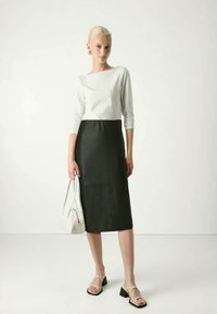 Γυναίκα με ξανθά μαλλιά, φορούσα λευκή μπλούζα με μακριά μανίκια, μαύρη τζίν φούστα μέχρι το γόνατο, μαύρες και λευκές ψηλοτάκουνες σανδάλες με λουράκια, κρατώντας μια λευκή τσάντα.