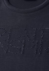 Schwarzes Baumwoll-T-Shirt mit Rundhalsausschnitt, das mit strukturierten, erhabenen Perlenverzierungen versehen ist, die "GREATER INSPIR" buchstabieren.