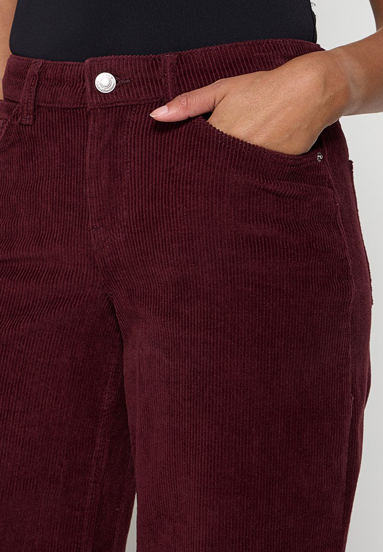 Bordeaux ribfluwelen broek met verticale ribstructuur, voorzien van voorzakken en een metalen knoopsluiting aan de taille.