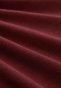 Burgunderfarbenes, strukturiertes Gewebe mit kleinen gewebten Mustern, das Falten aufweist, die einen wellenartigen Effekt erzeugen und Tiefe sowie Farbfülle zeigen.