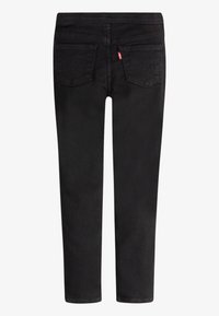 Des jeans en denim noir avec une coupe slim, un design à cinq poches et des coutures emblématiques sur les poches arrière. Le tissu a une texture lisse.