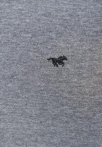 Tissu gris texturé avec un petit emblème de cheval brodé en noir centré sur la surface.