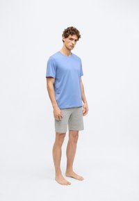 T-shirt de algodão azul claro com gola redonda e calções cinzentos, feitos de um tecido macio. O modelo está descalço, em pé contra um fundo liso.