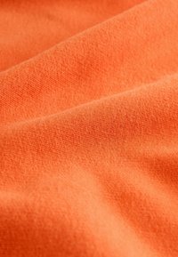 Oranž kangas pehme, tekstuurse pinna ja peente värvitoonide variatsioonidega, millel on voolav ja langev välimus.