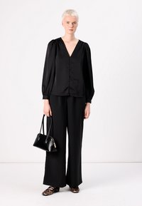 Blusa de seda negra con mangas largas abullonadas y escote en V, con botones en la parte delantera. Combinada con pantalones de pierna ancha negros y un bolso negro, complementada con unas bailarinas de leopardo.