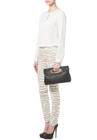 Femme portant un chemisier blanc à manches longues et un pantalon beige à imprimé zèbre, tenant un sac à main noir avec une anse dorée, portant des talons hauts noirs.