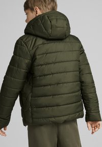 Grøn polstret jakke medhætte, med quilte struktur, vandrette sømme og en lomme med lynlås på siden. Glat materiale og tætsiddende design.