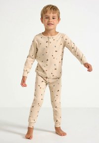 Beige ribstrikket pyjamasæt med lange ærmer og matchende bukser, med farverige blomsterprint overalt. Blød bomuldstekstur.