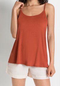 Top in rust color realizzato in tessuto morbido, con spalline sottili e vestibilità ampia. Abbinato a pantaloni corti chiari arrotolati.