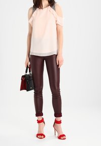 Světle růžová blůza s volány na rukávech, doplněná burgundskými legínami z umělé kůže. Doplňky zahrnují černou kabelku a červené sandály na chlupatém podpatku.