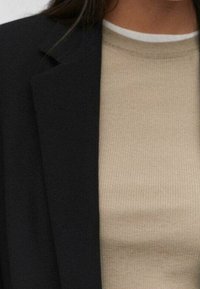 Mustapuku beige-raidoituksella varustetun pyöreäkauluksisen neuleen päällä, jonka ylhäältä pilkottaa kerrostettu valkoinen kaulus.