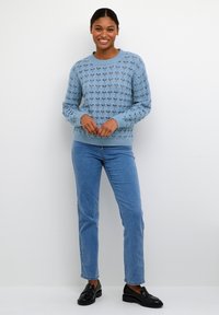 Ljusblå stickad tröja med ett strukturerat mönster, rund hals, och ribbade ärmslut, ihop med ljusblå jeans och svarta loafers.