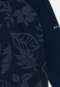 Jūras zila garenrāvējo krekls ar smalku lapu rakstu. Izgatavots no mīkstas auduma, ar kontrastējošu plecu šuvju un logo detaļu uz piedurknes.