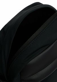 Bolso negro con un exterior suave y texturizado, con un acento de cuero liso y cierre de cremallera. Diseño minimalista con una parte superior plegable.