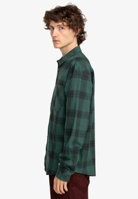 Grønternet flannel skjorte med lange ærmer, knappet krave, brystlomme og mørkegrå detaljer. Fremstillet af blødt, struktureret stof.